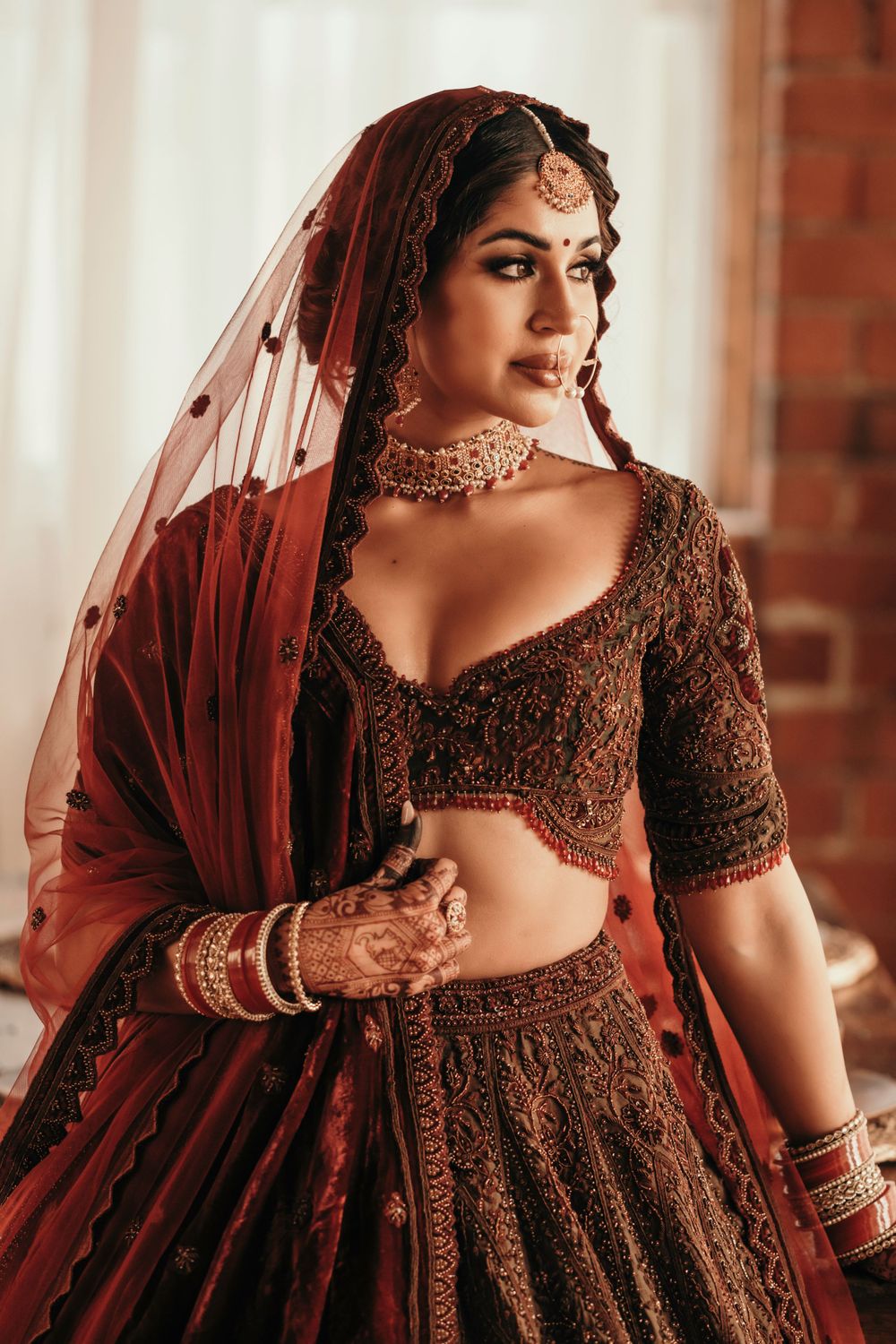 Traditional Indian bridal attire featuring an ornate brown lehenga with detailed embroidery and red dupatta.