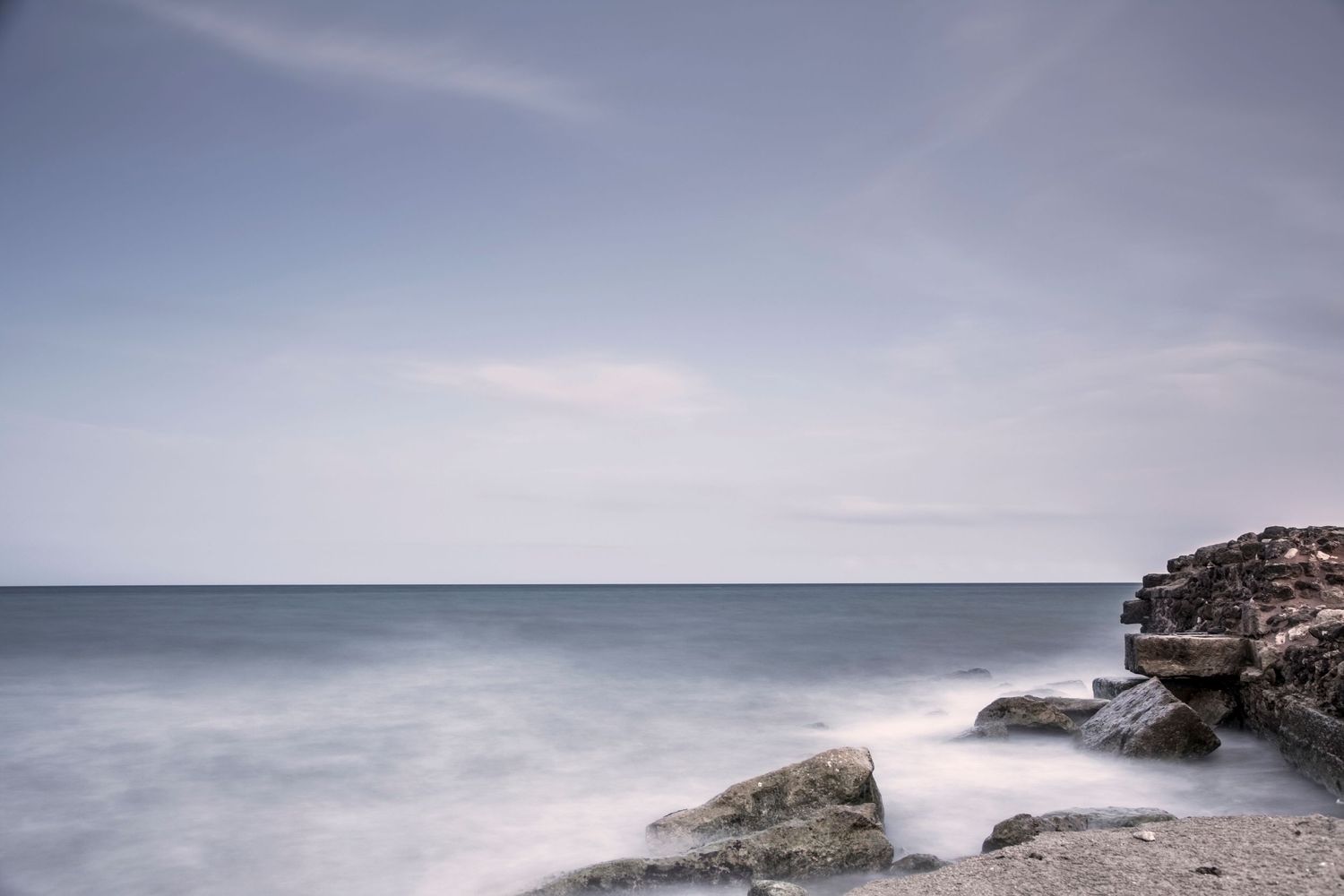 Misty seascape with large rocks and crashing waves against a moody gray sky along the coastline.