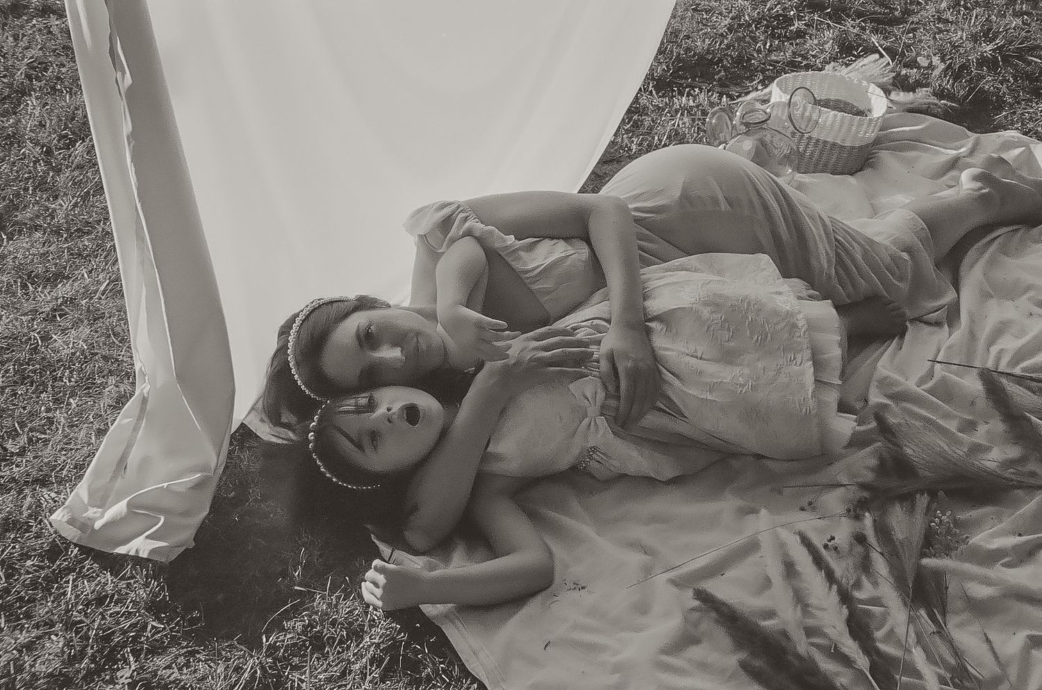People lying on grass wearing light-colored dresses in a dreamy black and white photograph.