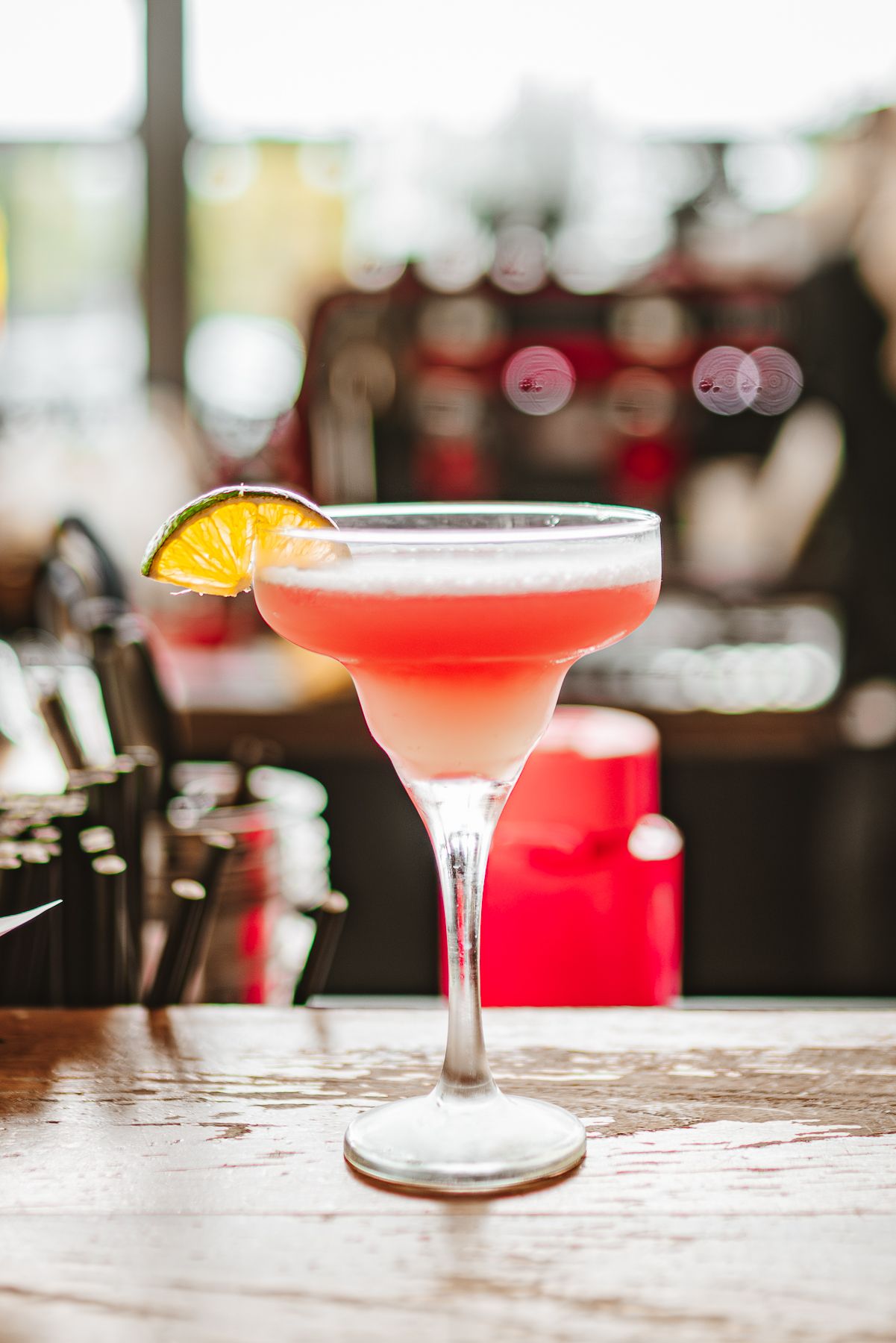 Pink cocktail with orange garnish in martini glass on wooden bar counter taken during a food styling and brand photoshoot in Melbourne cafe