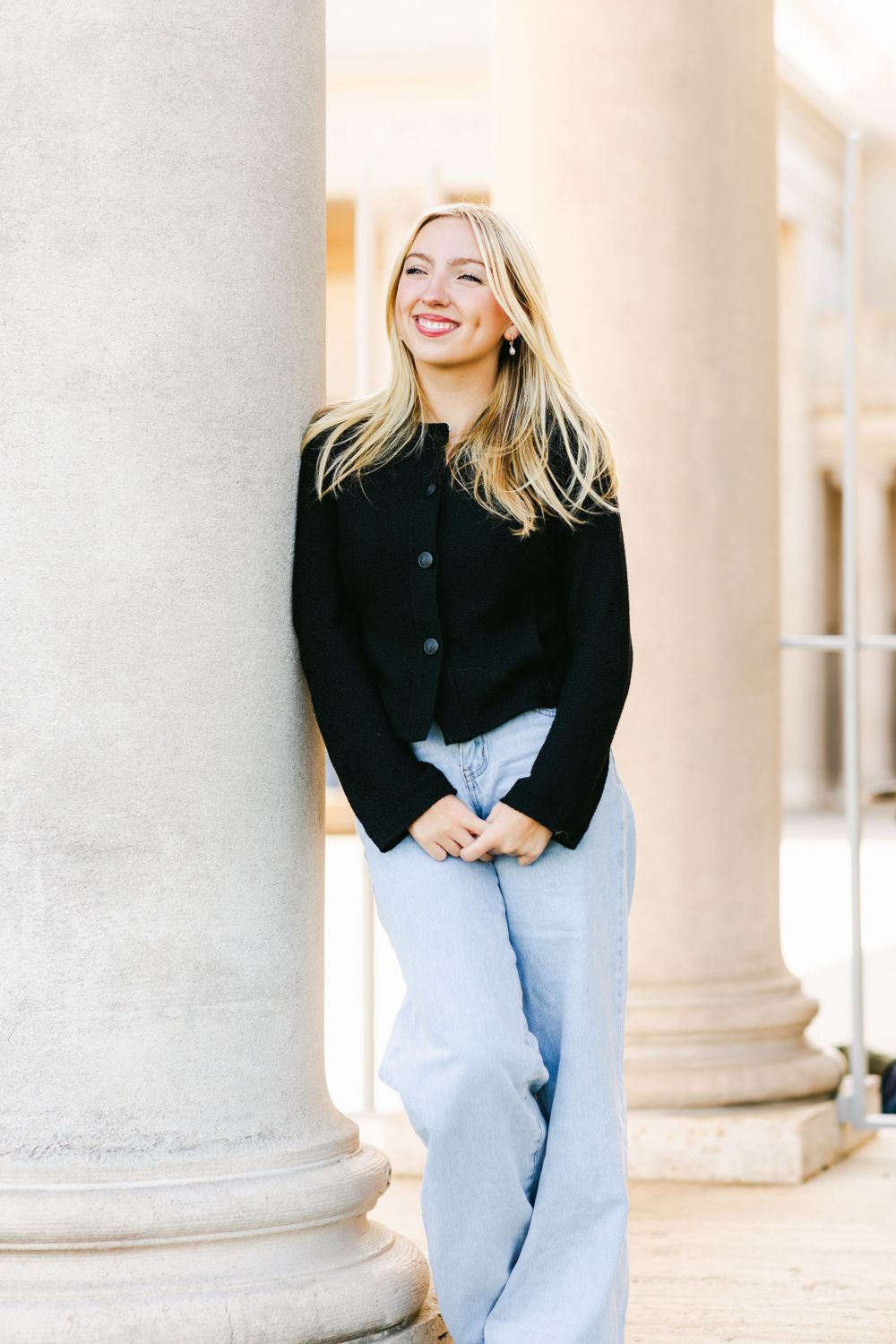 Stylish casual outfit with black cardigan and light-wash jeans in front of architectural stone columns.By Chelsee Rawe Photography.