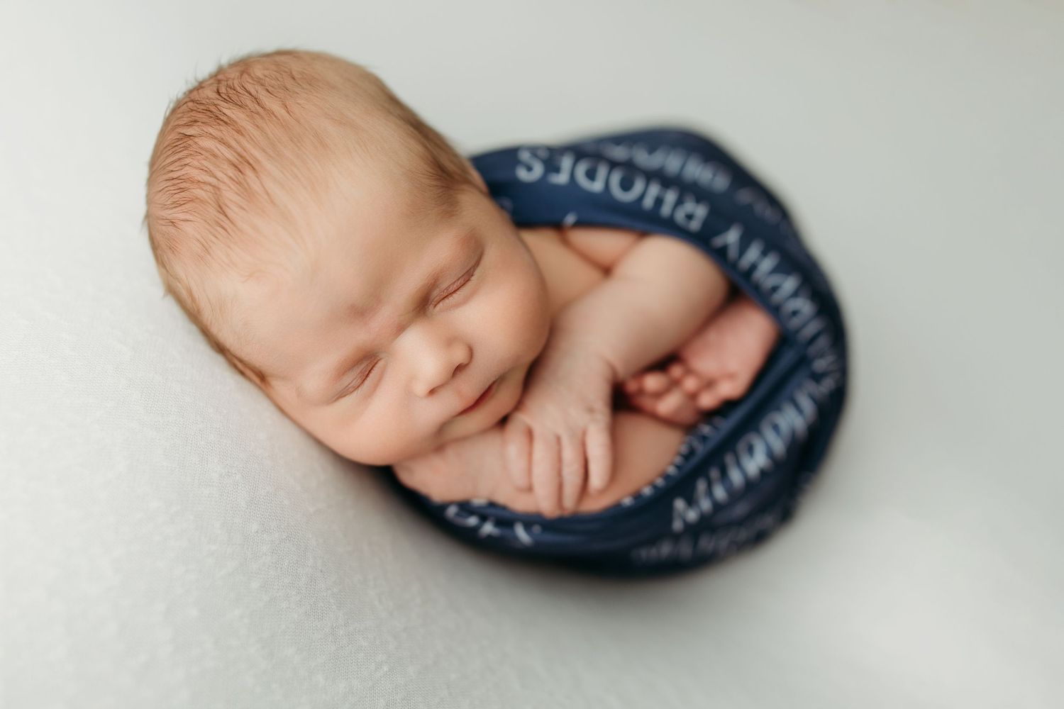 Sleeping newborn wearing customized navy wrap posed against white background.