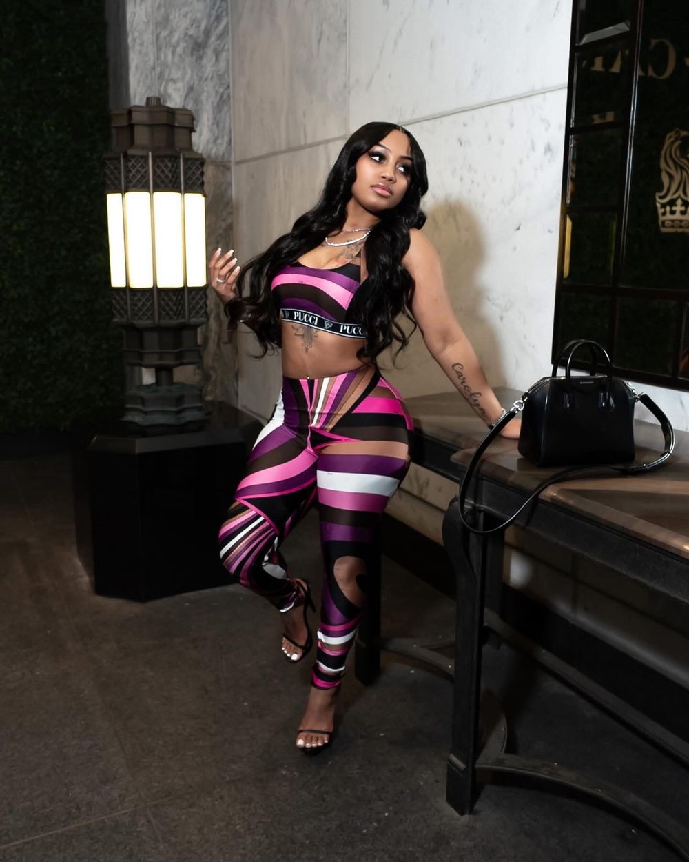Model in pink and black striped athletic wear poses in industrial setting.