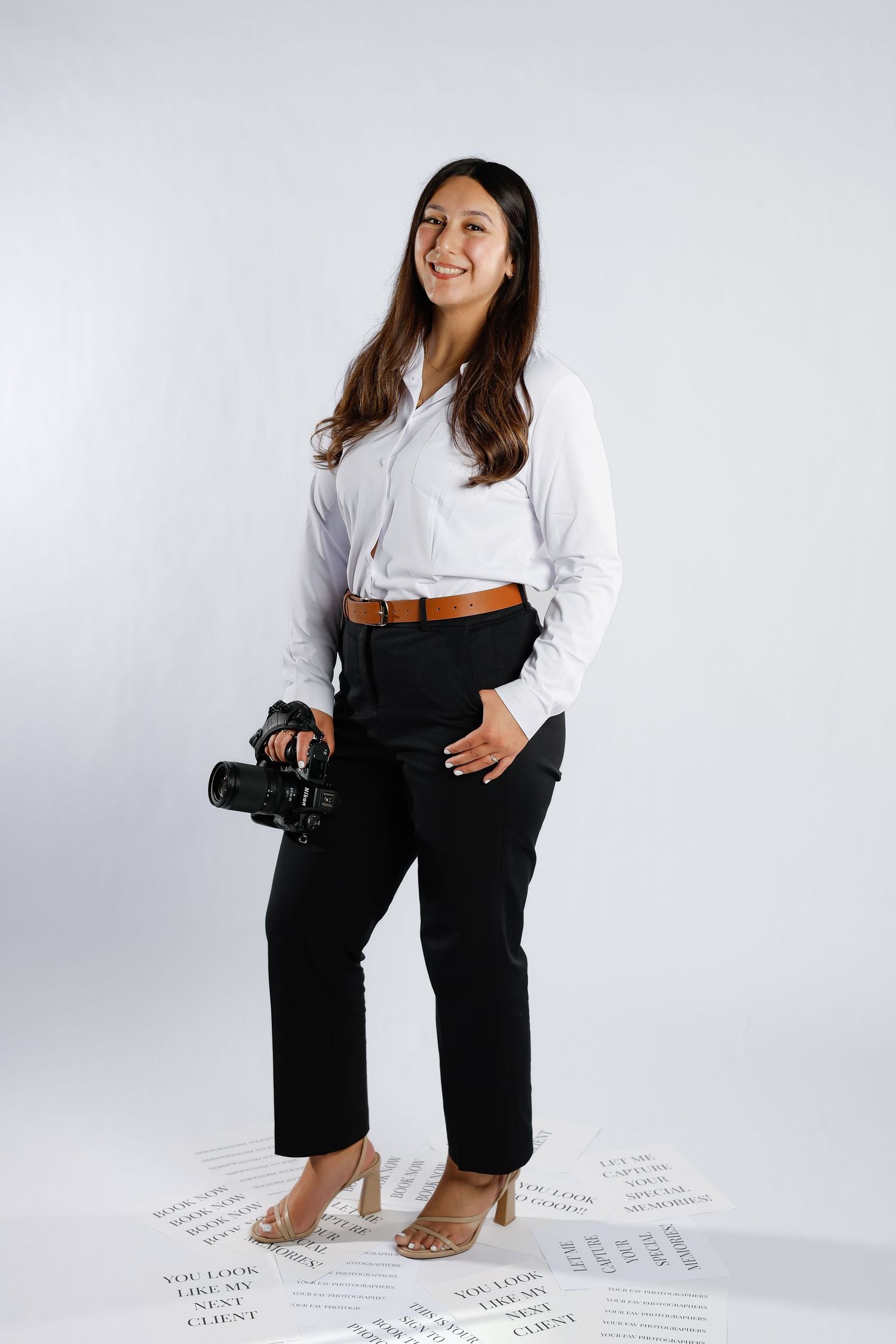 Professional photographer poses with camera against white background in studio setting.