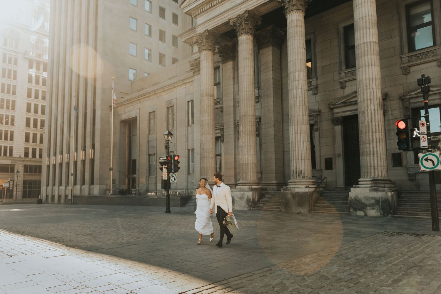 Two figures walk near grand neoclassical columns of historic building with tall architecture in background.