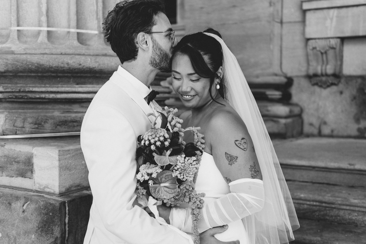 A joyful black and white wedding photograph showing a tender embrace and shared smile on stone steps.