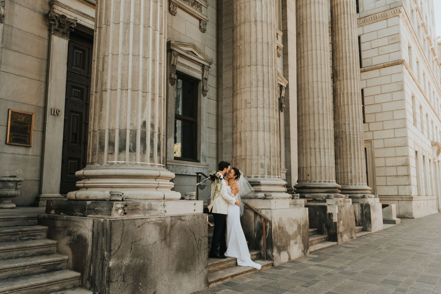 A couple shares a tender moment between grand stone columns at the entrance of a historic building.
