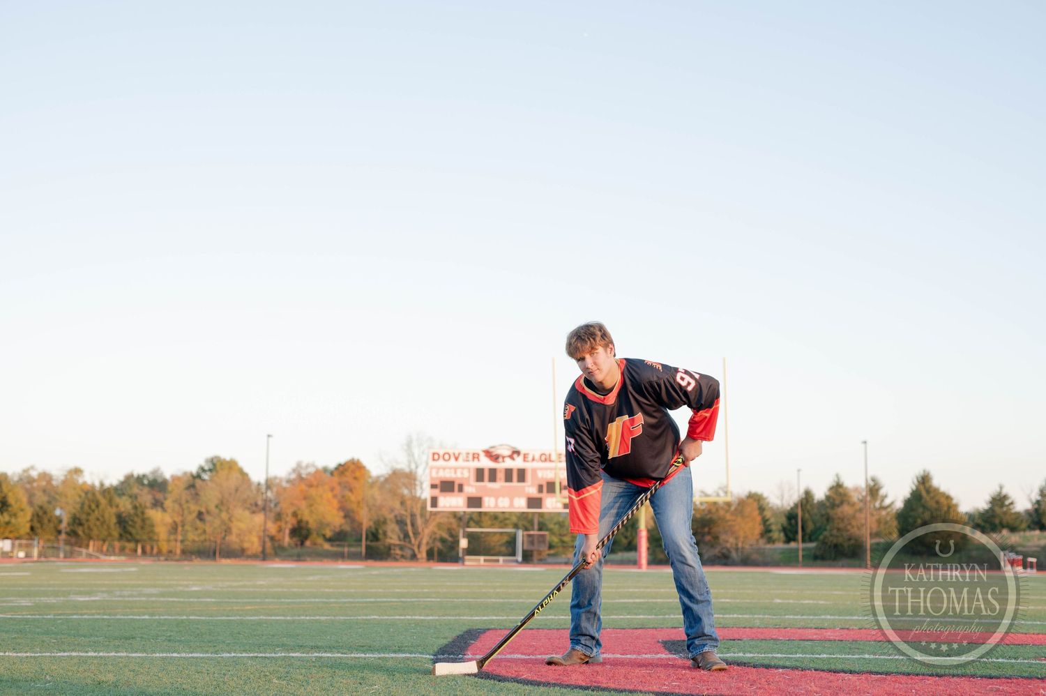 Athlete practices hockey stance on red turf field during sunset.