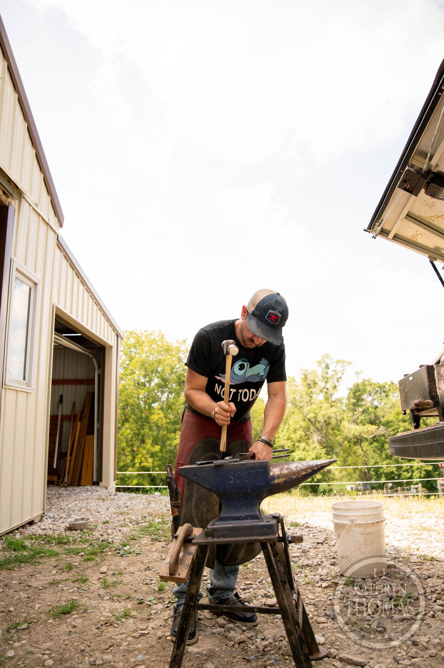 Farrier hammering metal on an anvil outside a horse barn.