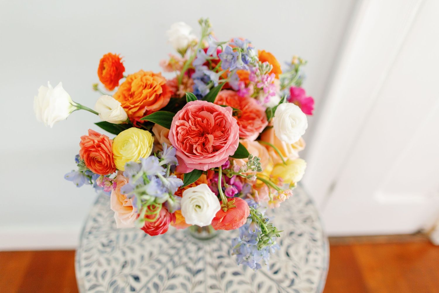Colorful garden roses in orange, pink and yellow arranged with blue wildflowers in an ornate crystal vase.