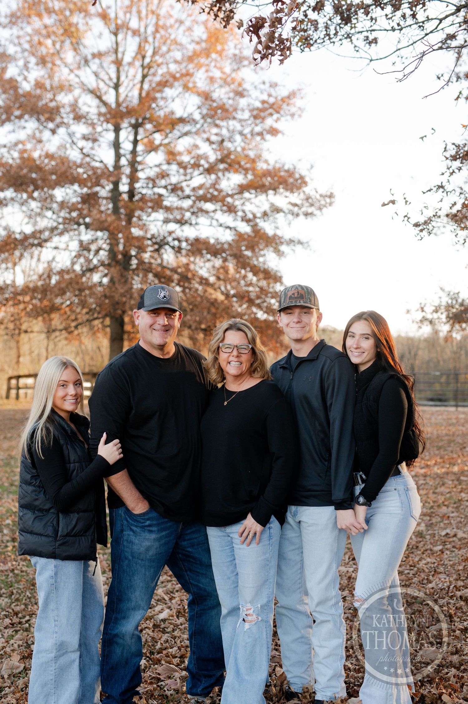 A family group poses casually together in a fall setting wearing coordinated black tops and jeans.