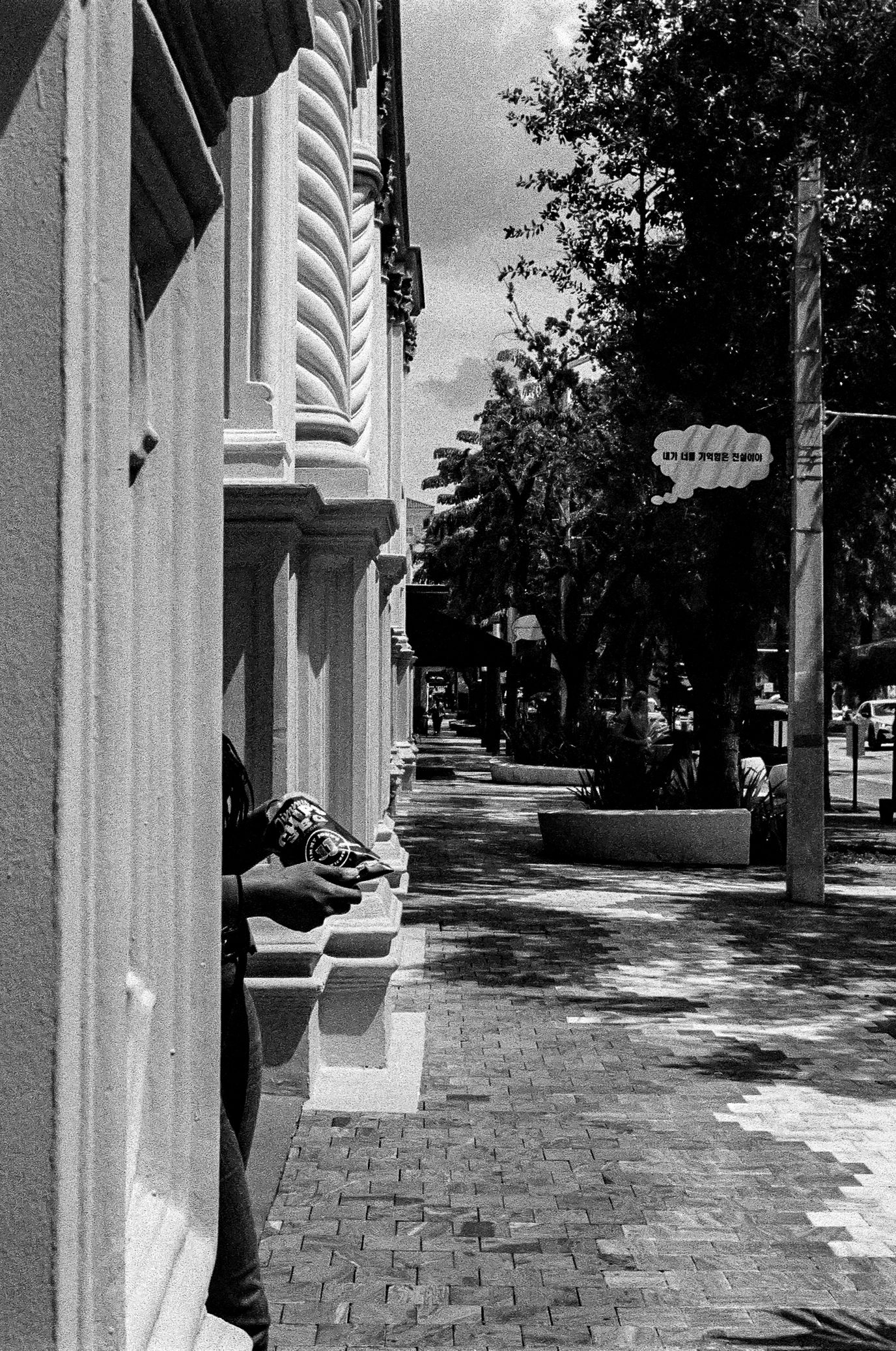 A black and white street scene showing ornate white architectural details and a brick sidewalk in an urban setting.