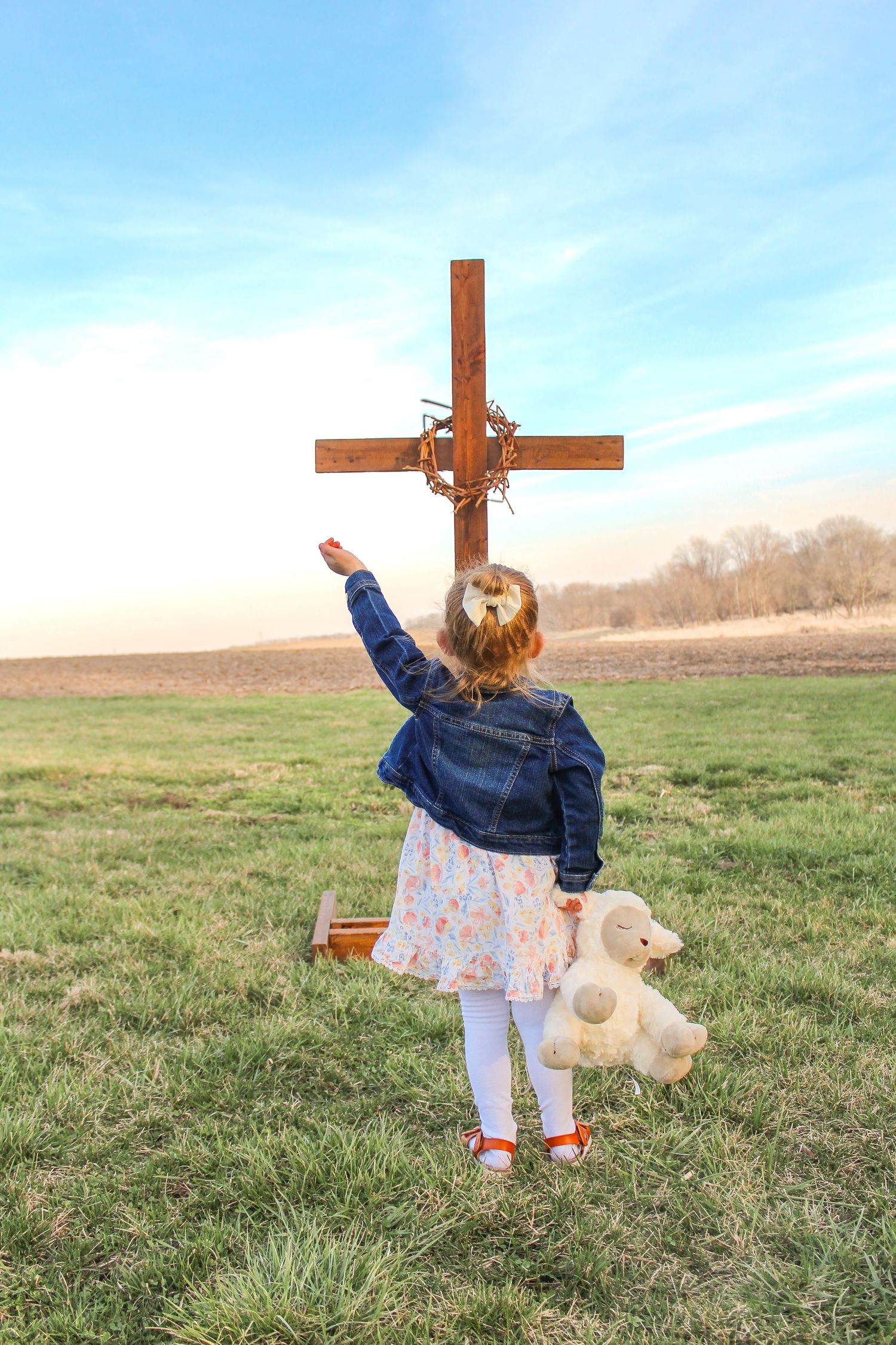 Springfield, IL family photographer captures a young girl with her hand raised while standing in front of a wooden cross.