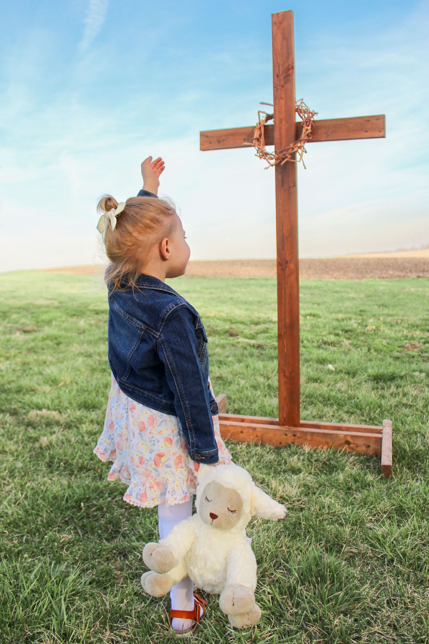 Springfield, IL family photographer captures a young girl with her hand raised while standing in front of a wooden cross.