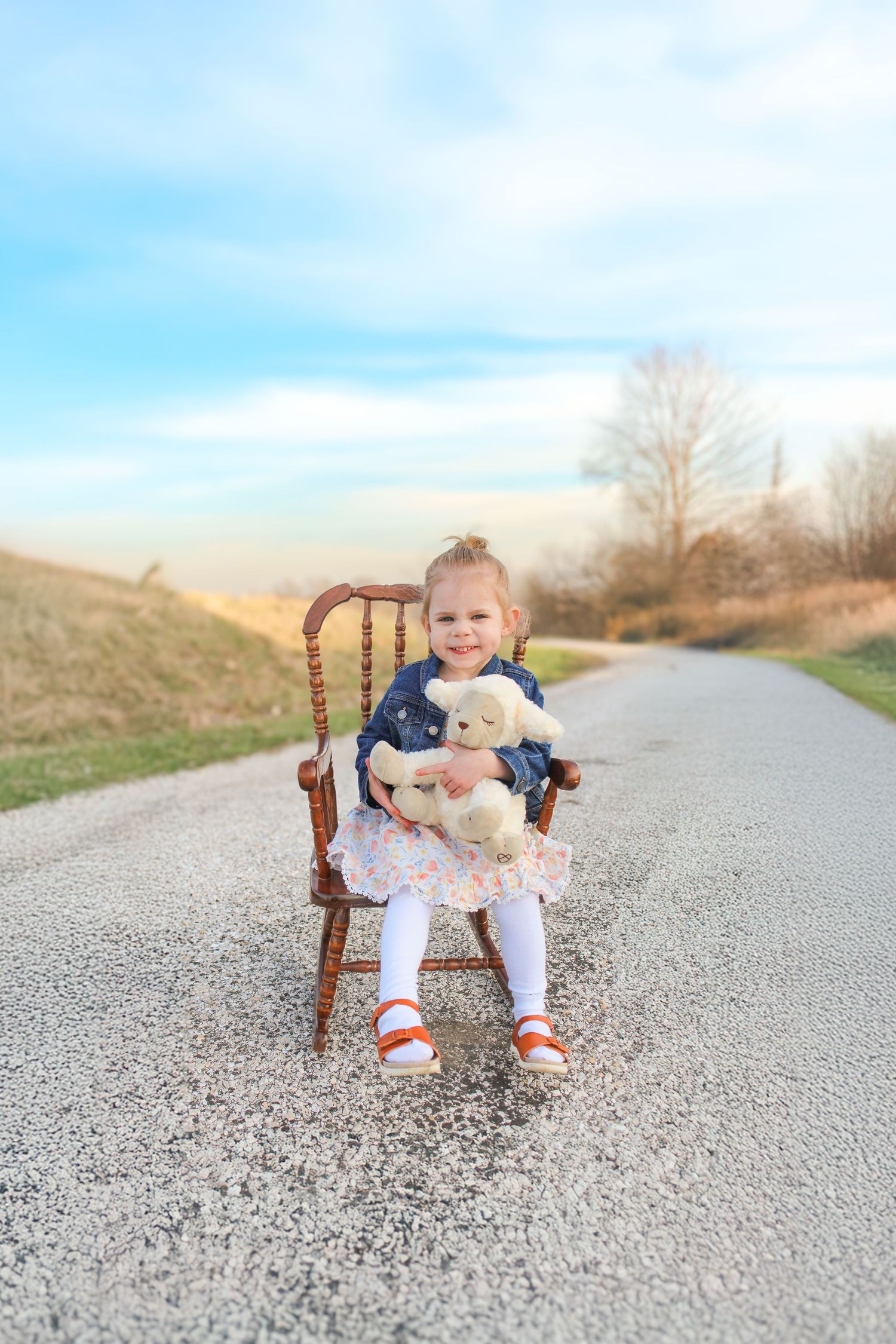 Springfield, IL photographer captures a young girl sitting on a small rocking chair on a gravel lane while holding a stuffed lamb.
