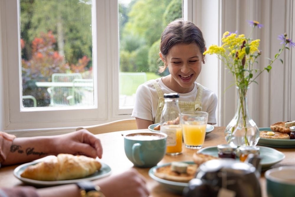 Family enjoying breakfast together with croissants, orange juice and coffee at a bright dining table with yellow flowers.