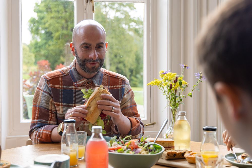 Person enjoying a meal at a brightly lit dining table with yellow flowers in a vase and various dishes.