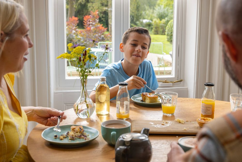 People enjoying a casual brunch together around a sunny window with orange juice and flowers on the table.