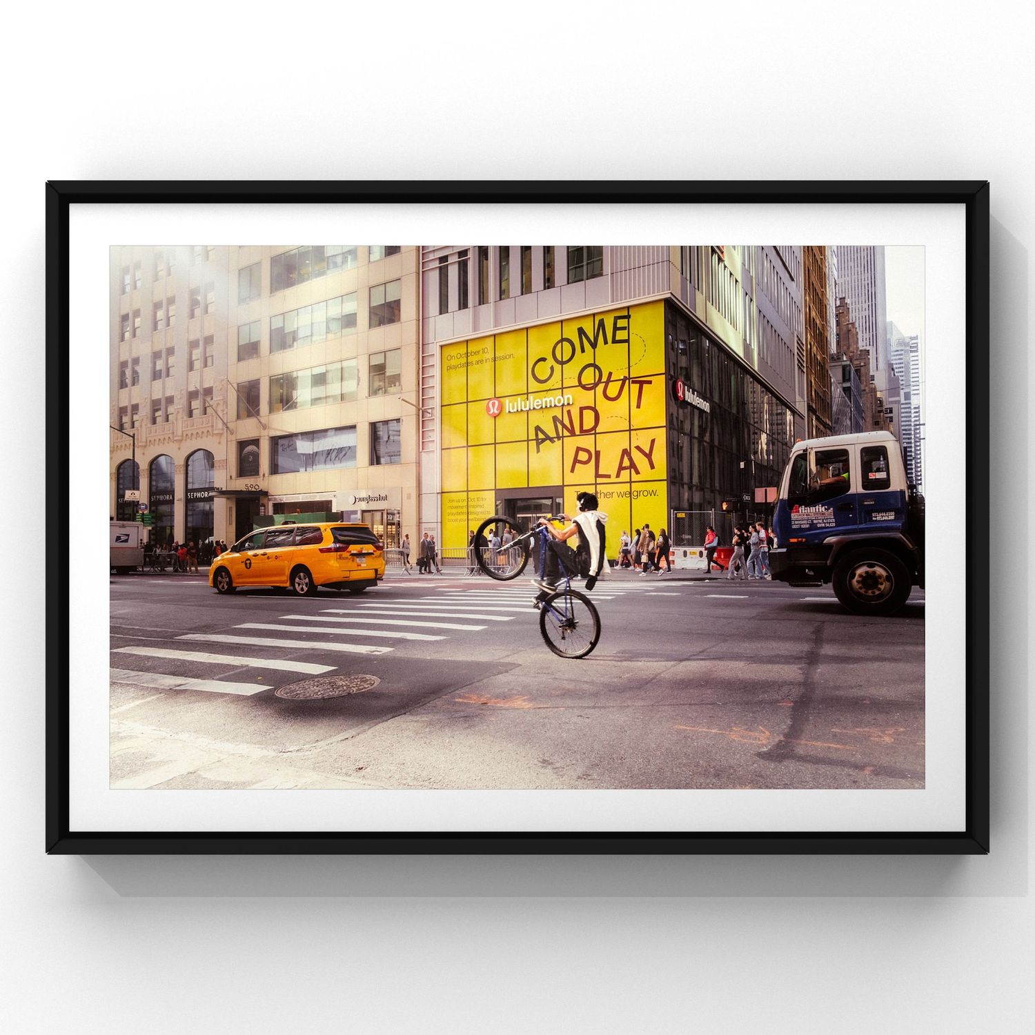 A cyclist performs a wheelie on a city street with yellow taxi and bright graffiti wall in the background.
