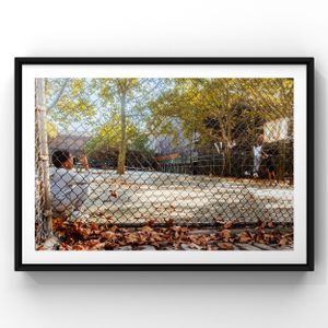 Chain link fence surrounds an empty baseball field with fallen autumn leaves scattered on the ground in a park setting.