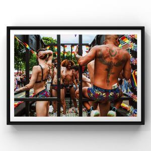 Shirtless parade participants wearing swim shorts climb metal bars during a festive outdoor celebration.