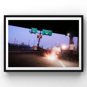 Firework sparks illuminate a dark highway with illuminated road signs at night during a dusk moment.