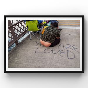"CARS LOVED" graffiti written in blue chalk on concrete sidewalk next to a green folding chair and potted plant.