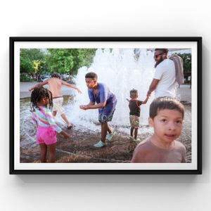 Children and adults play together in a fountain splash pad on a warm summer day.