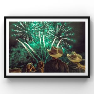People wearing cowboy hats watch green fireworks light up the night sky during an outdoor celebration.