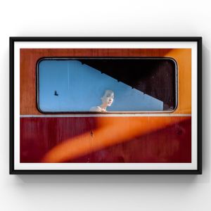 Art photograph through a train window showing figure in silhouette against blue sky with diagonal orange light beam.