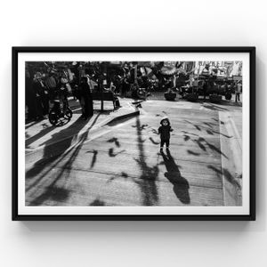 Black and white artistic photograph capturing long shadows cast on pavement by a crowd gathered in an urban setting.