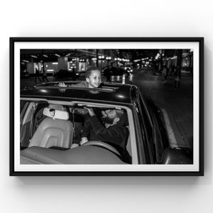 A black and white nighttime photograph showing the interior view of a vehicle with passengers on a city street.
