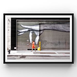 A figure in bright orange walks past a large fashion advertisement display on a modern urban storefront.
