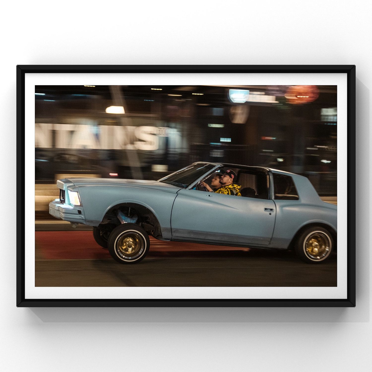 A light blue lowrider car with hydraulics bounces on city streets at night in a dynamic motion shot.