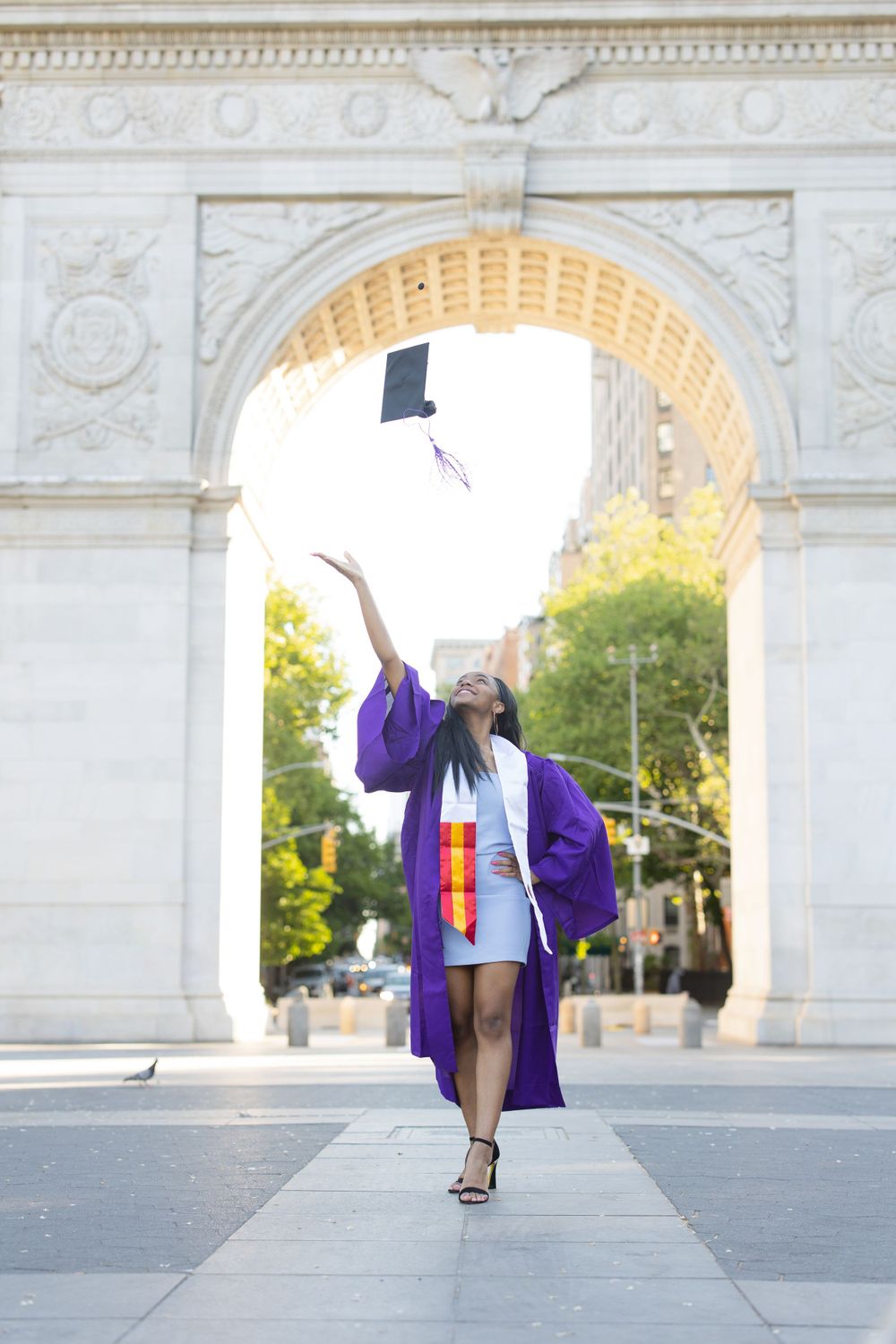 Graduate tosses cap while wearing purple graduation gown under Washington Square Arch.