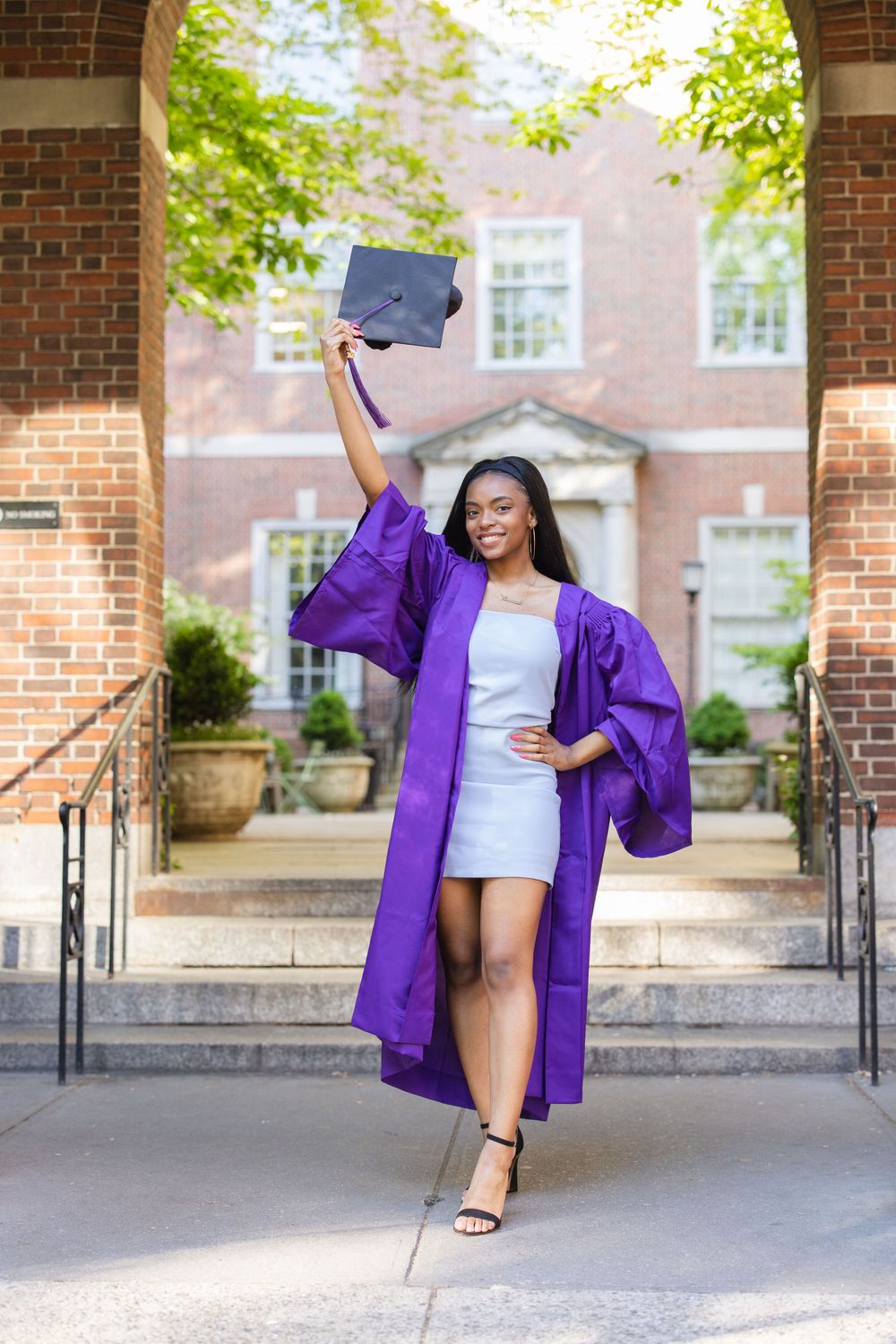 Graduate in purple commencement robe celebrates on campus steps with diploma.