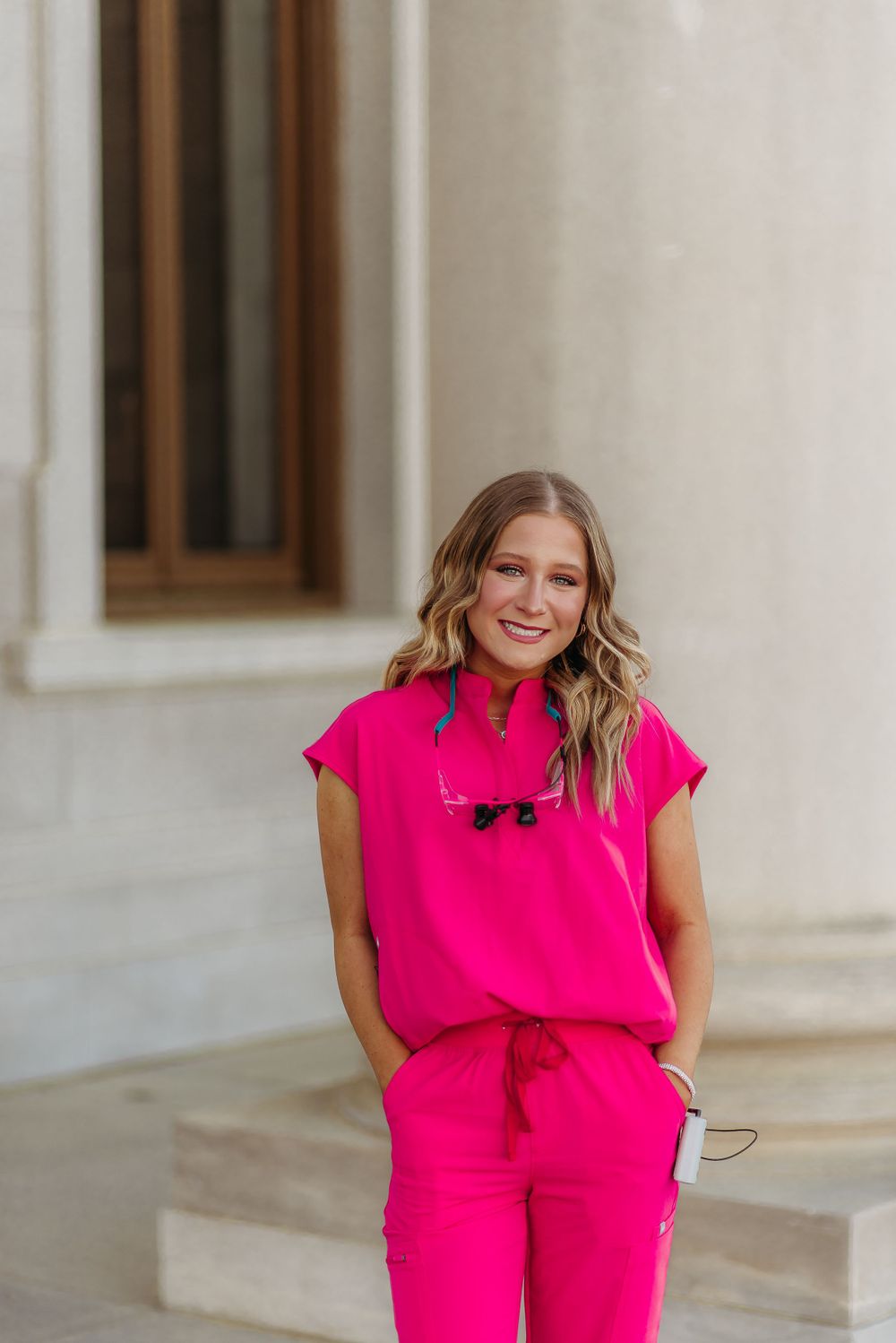 Person wearing hot pink athleisure outfit stands against white building exterior.