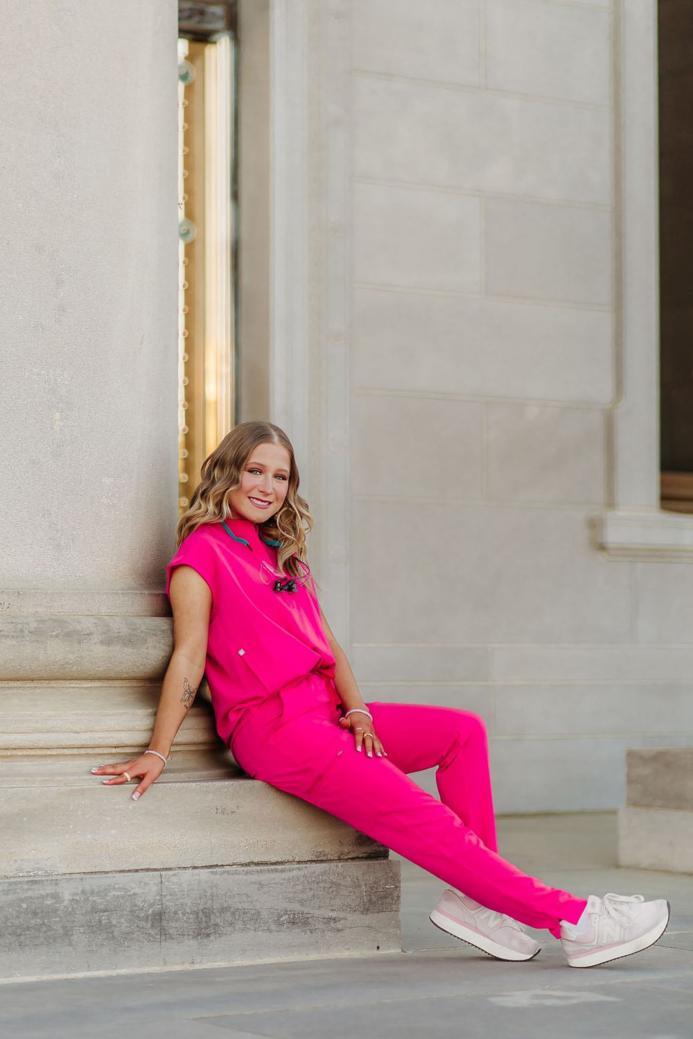 Someone in bright pink loungewear relaxes on stone steps of a building.