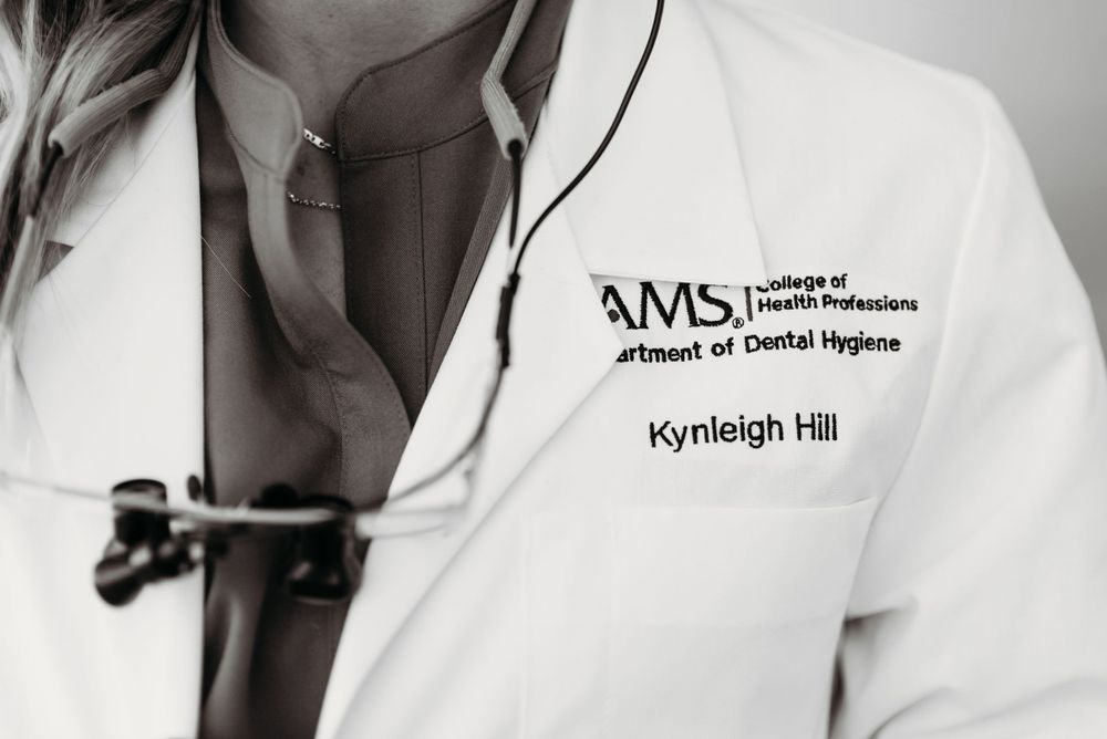 Close-up view of a white medical coat with embroidered UAMS healthcare branding and text.