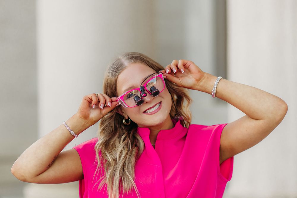 Person wearing hot pink scrubs and fun sunglasses poses playfully outdoors.