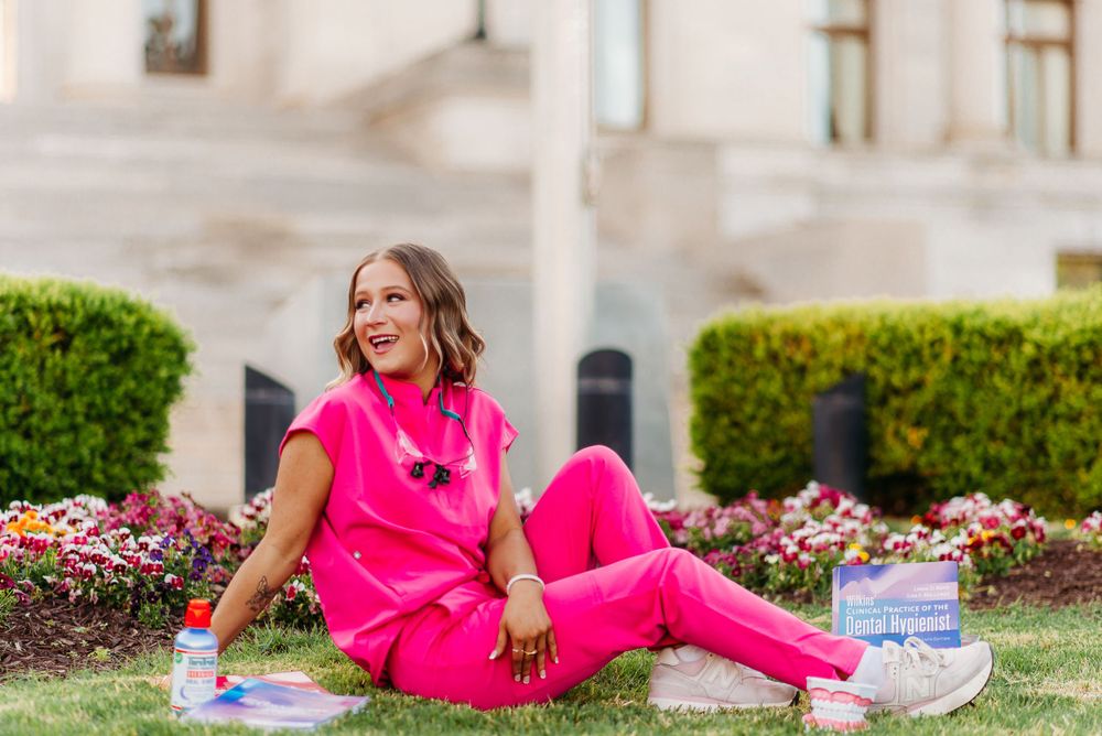 Person relaxing on grass wearing bright pink medical scrubs near blooming flowers.