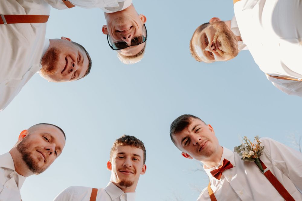 Fun low angle shot of groomsmen forming circle looking down at camera against blue sky.