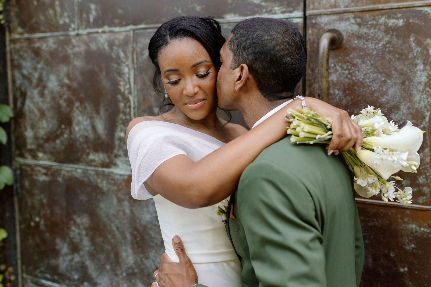A romantic moment shared between a couple on their wedding day with white flowers against a stone wall background.