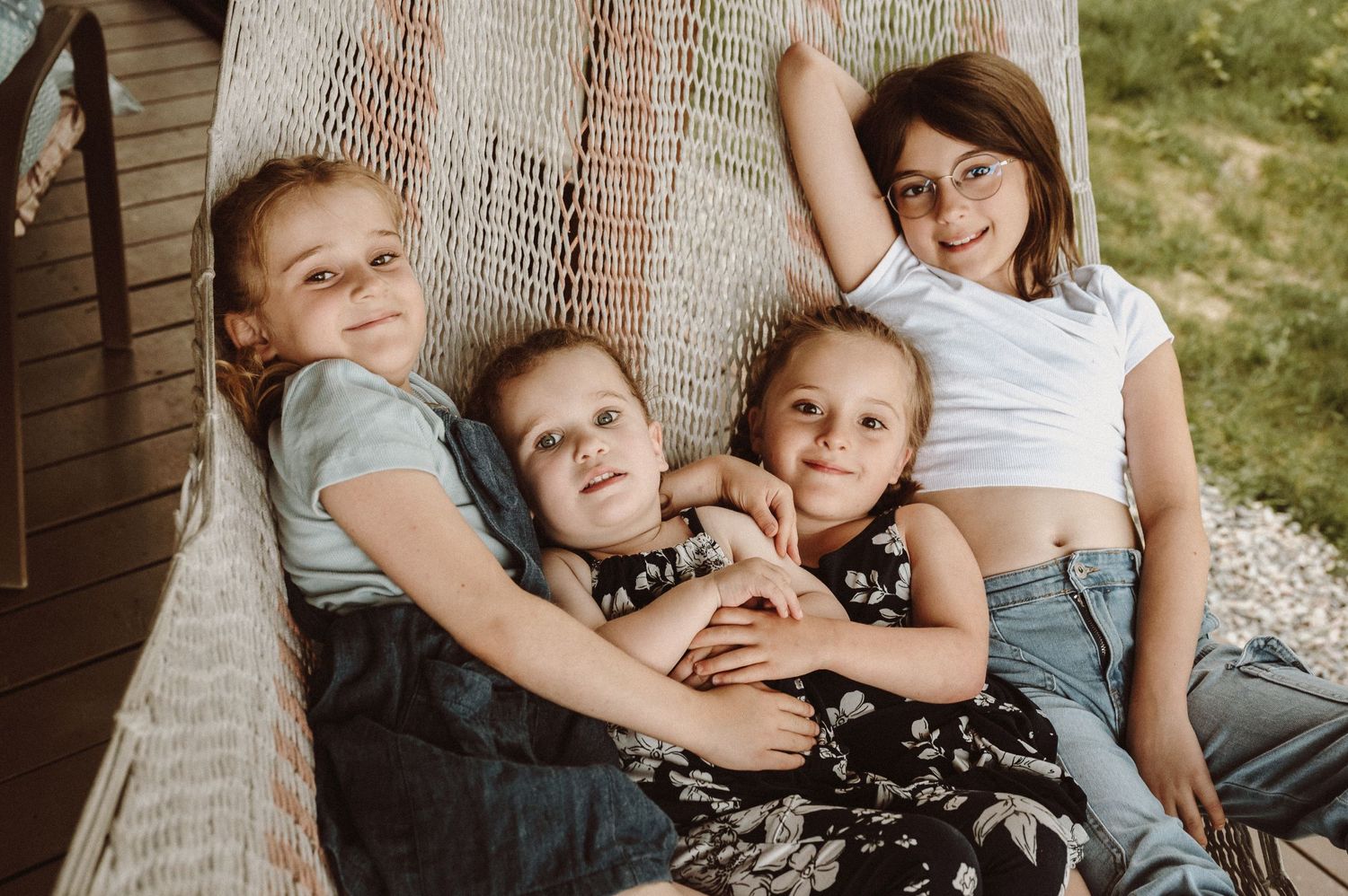 Four children lounging together in a hammock during a sunny outdoor photoshoot.