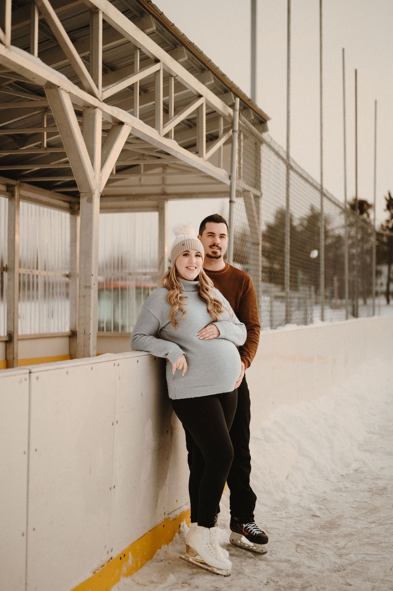 A couple poses against a wooden structure in winter setting.