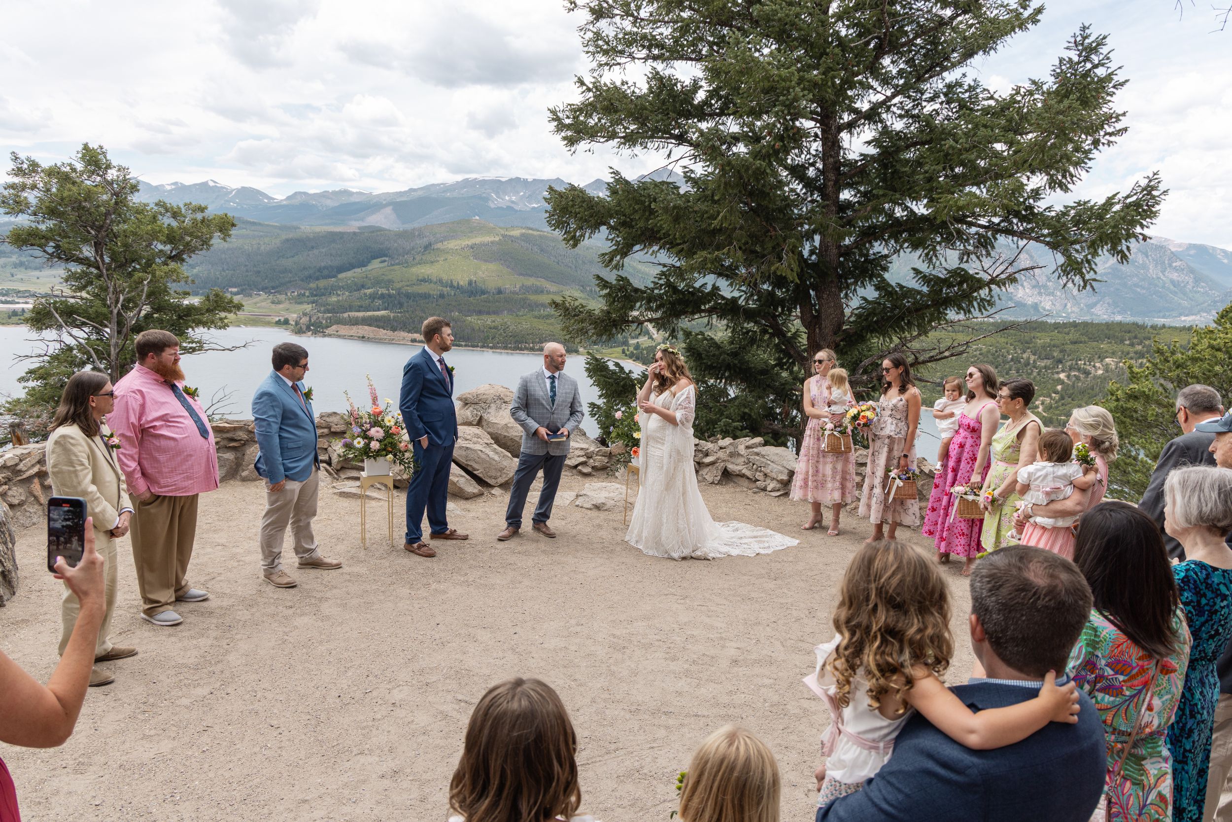 Wedding ceremony guests gather on a scenic mountain viewpoint overlooking a dramatic valley landscape.