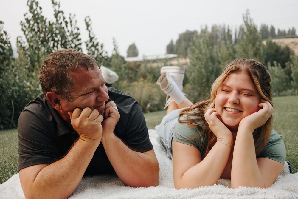 A couple lying on a blanket outdoors sharing a playful moment together.