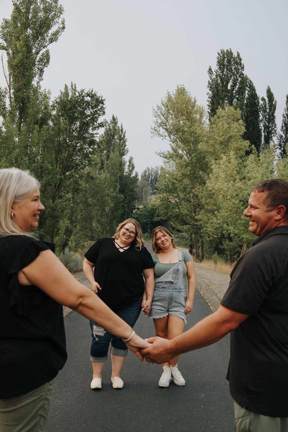 Two couples sharing laughs on a tree-lined path during an outdoor photoshoot.