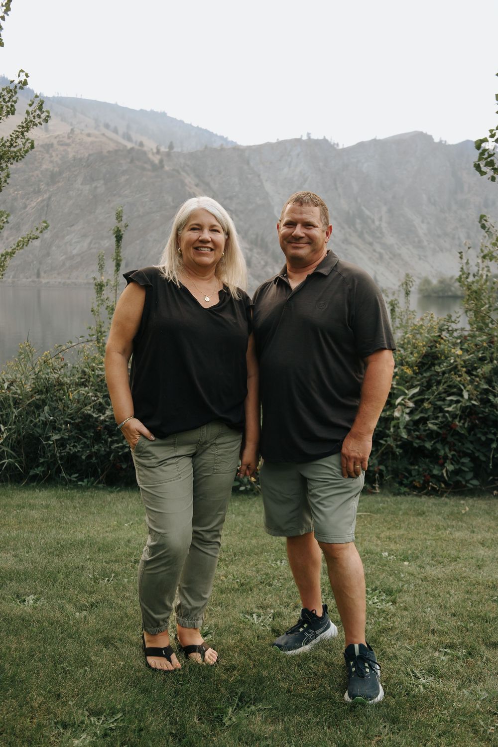 A couple standing together outdoors with mountains and lake in the background.