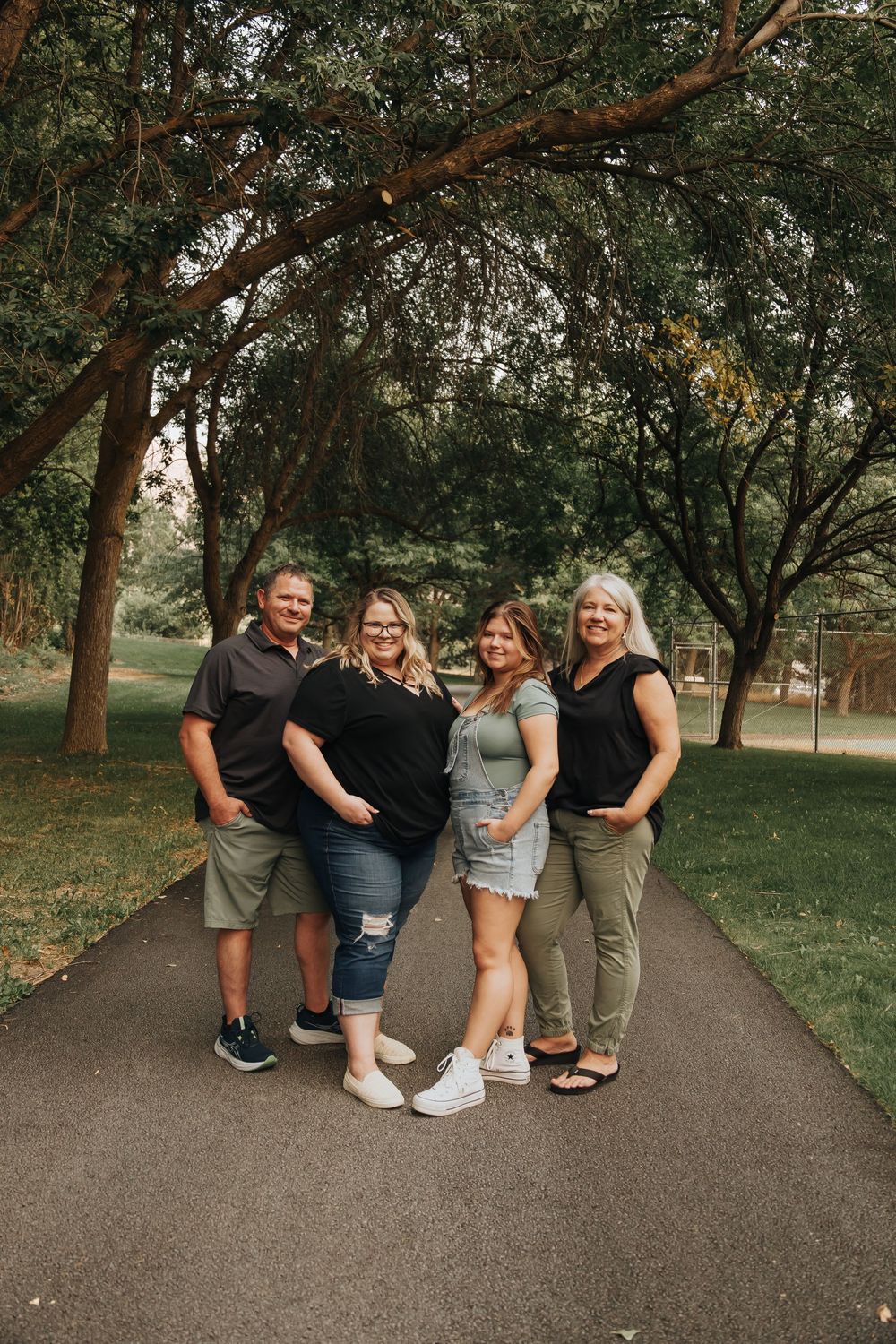 Group of four people posing together on a tree-lined path during summer.